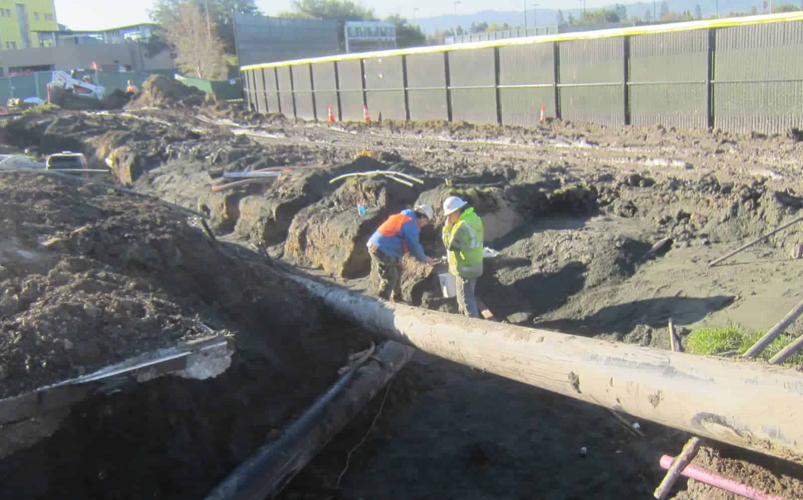 Construction workers diligently repairing a pipe buried in the dirt at a construction site.